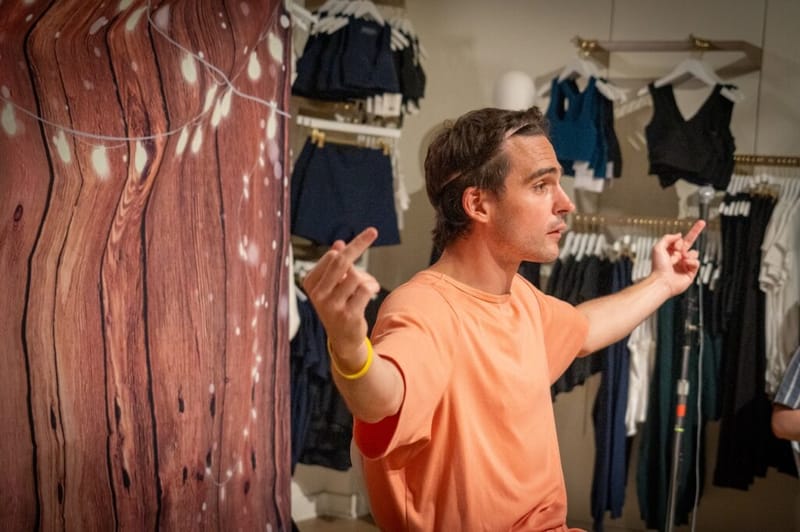 Dan Lerman performs a comedy bit, gesturing with both hands, at the Beyond Yoga venue.
