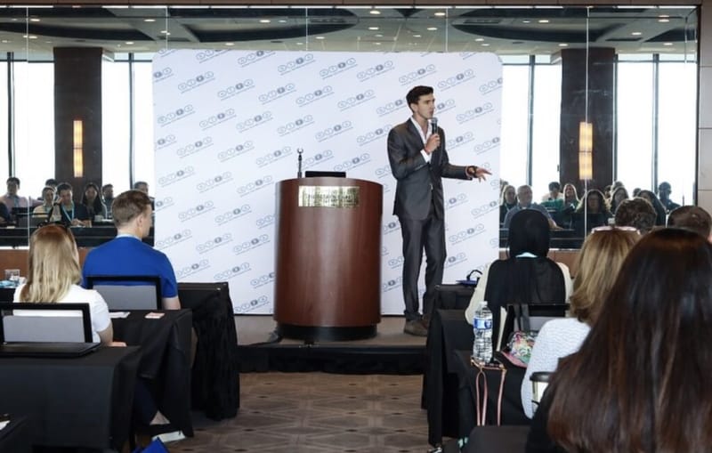 Dan Lerman speaks to a conference audience, microphone in hand, beside a podium.