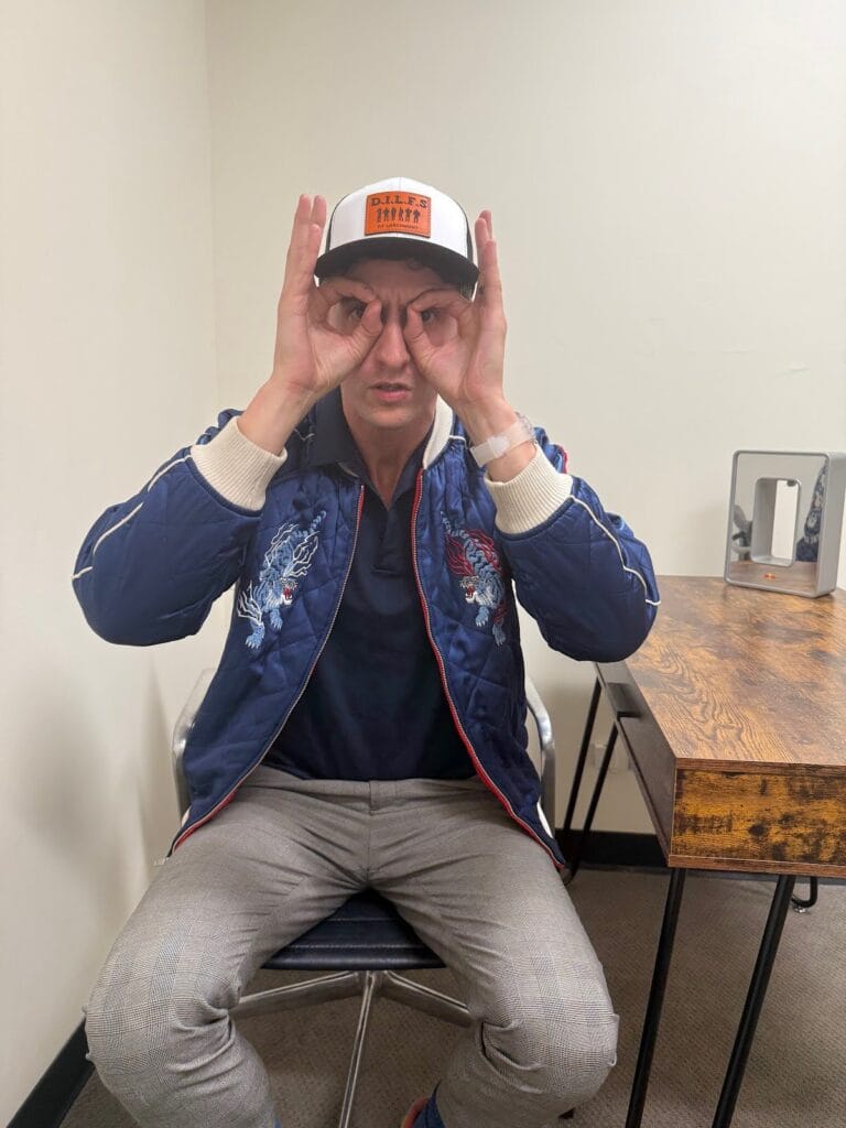 Dan Lerman wears a 'DILFs of Larchmont' cap and makes a binoculars gesture over his eyes.