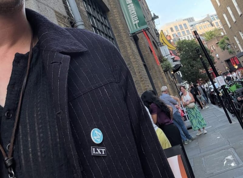 Close-up of a League of Exceptional Tutors lapel pin on a pinstripe blazer on a London street.