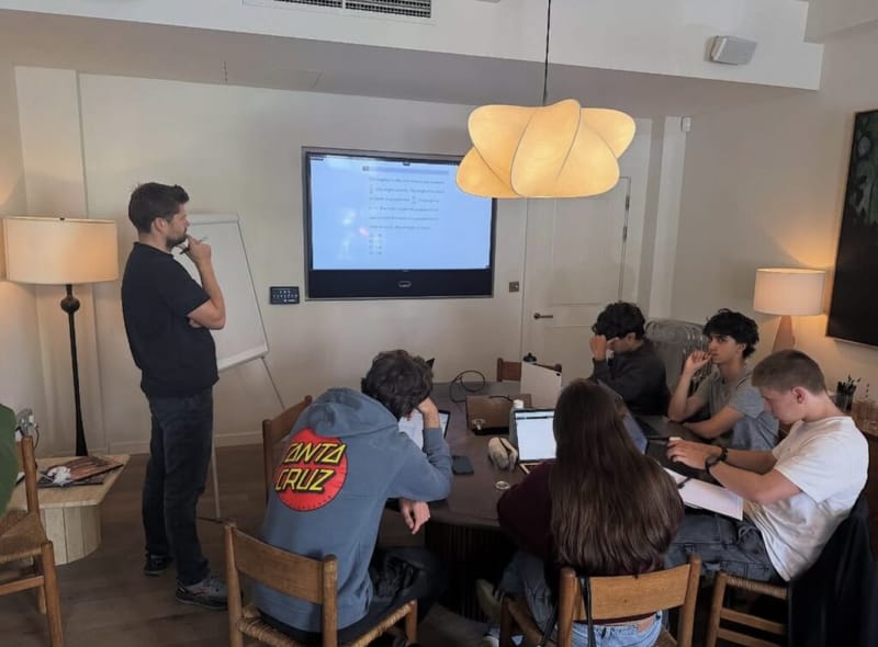 Dan Lerman leads an SAT boot camp session in London as students work at a table, an SAT question on the screen behind him.